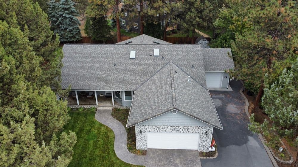 Aerial view of a modern home surrounded by trees, featuring a stone accent facade and driveway.