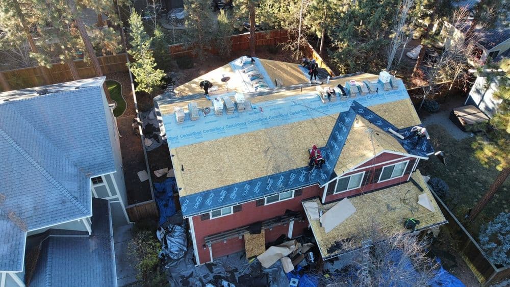 Roof replacement in progress on a red house, with workers installing materials on the rooftop.