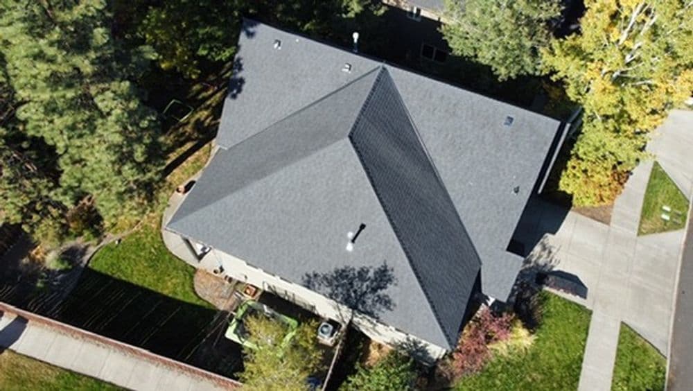 Aerial view of a modern home with a dark shingle roof and landscaped garden.