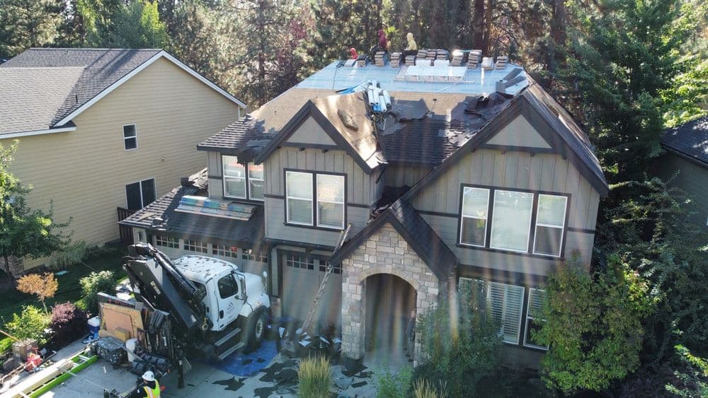 Roof replacement in progress on a large suburban house with workers and equipment visible.