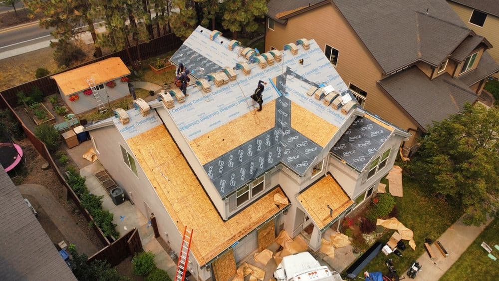 Workers installing a new roof on a residential home, surrounded by roofing materials.