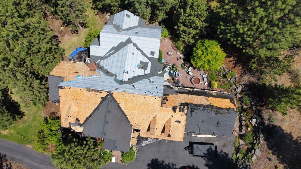 Aerial view of a house undergoing roof repairs with surrounding trees and landscaping.