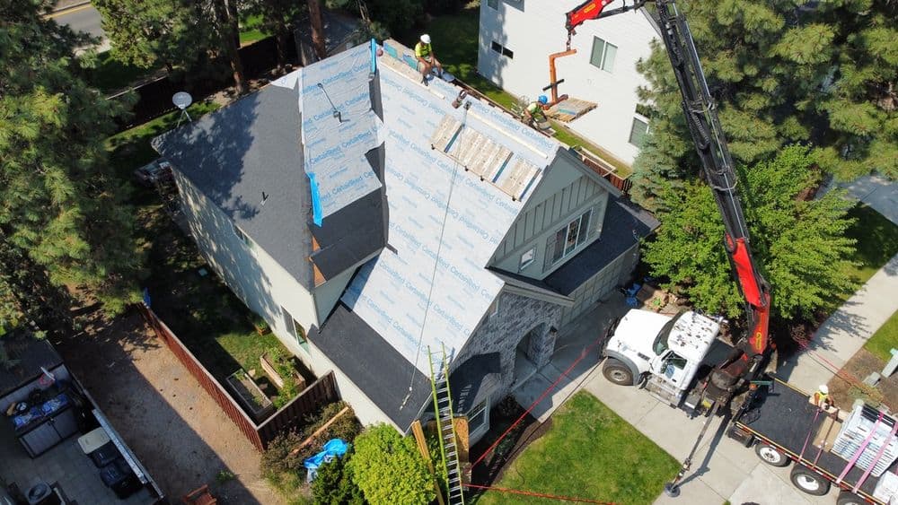 Roofing installation in progress on a house, with workers and equipment visible.