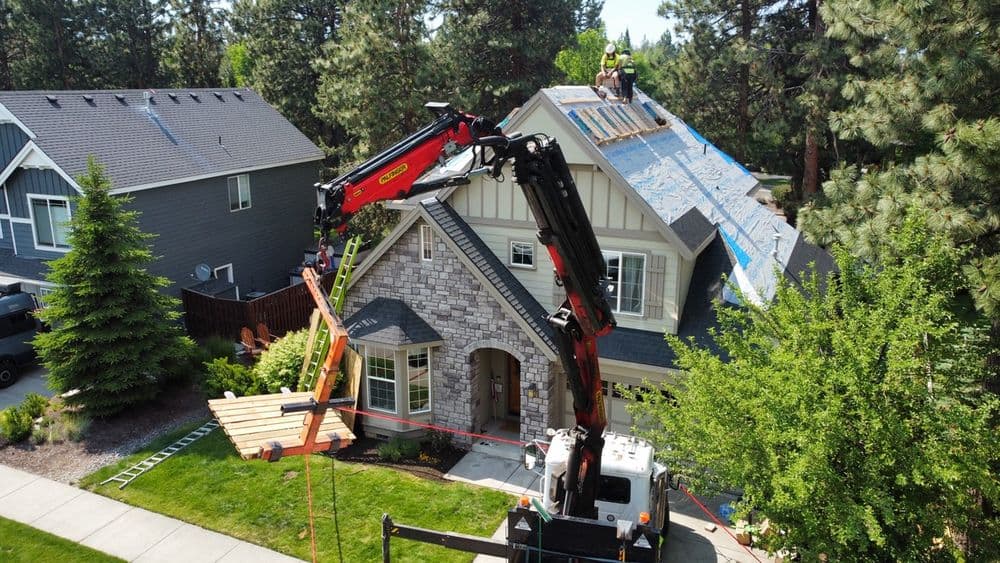 Roofing crew using a crane to lift materials onto a residential home in a suburban neighborhood.