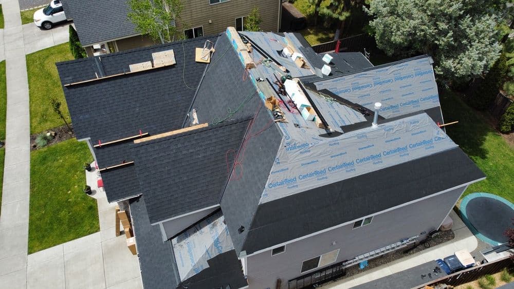 Aerial view of residential roofing under construction with black shingles and protective covering.