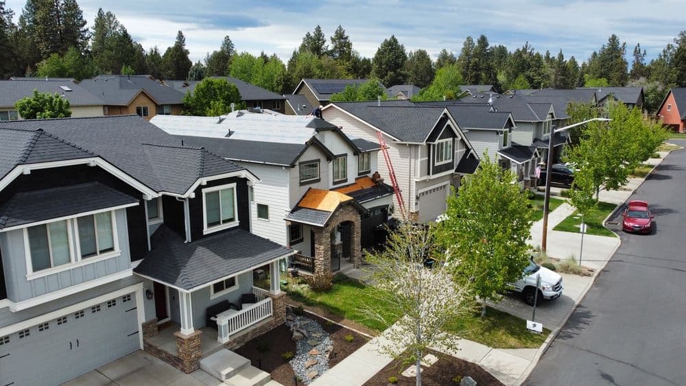 Roofing installation on suburban homes with green trees and quiet street view.