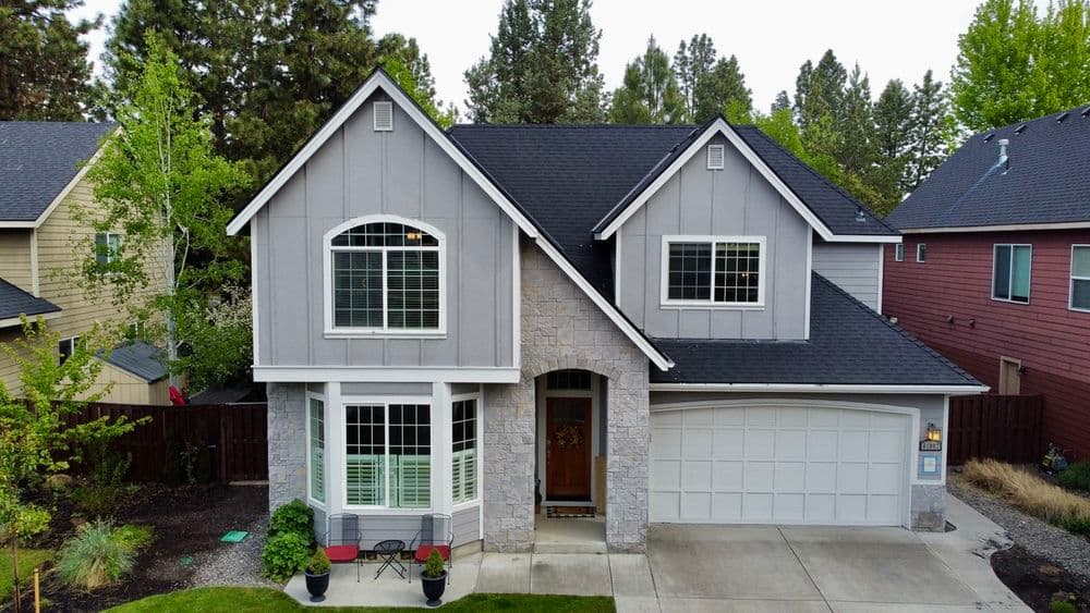 Modern gray suburban home with large windows, stone accents, and a two-car garage.