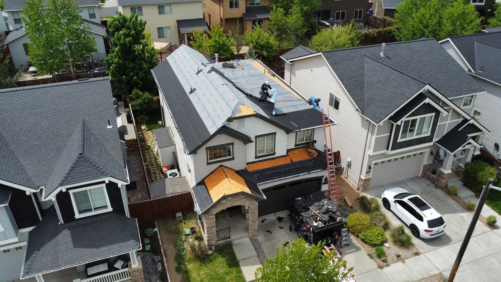 Aerial view of a house undergoing roof installation with workers and equipment on site.