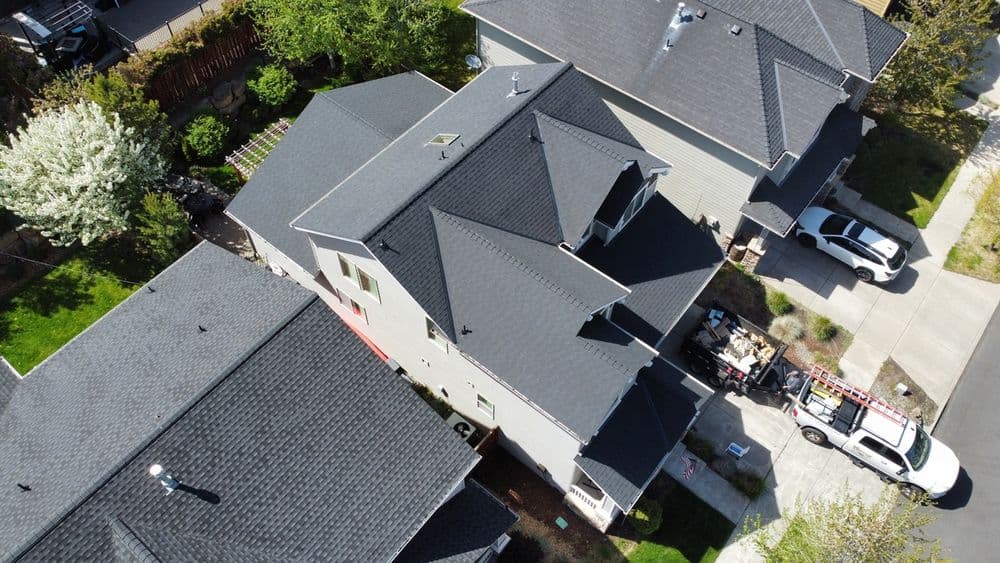 Aerial view of residential roofs with dark shingles and surrounding greenery.