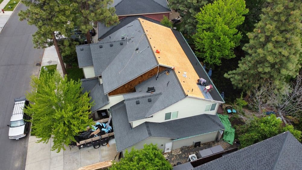 Aerial view of a house undergoing roof replacement with workers and tools visible.