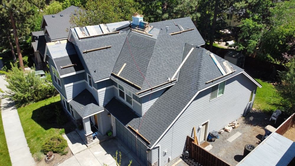 Aerial view of a house undergoing roof renovations with new shingles being installed.