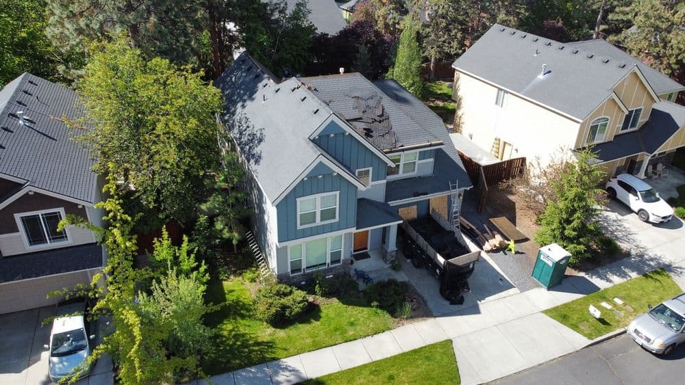 Aerial view of a residential home with a blue exterior, landscaping, and construction debris.