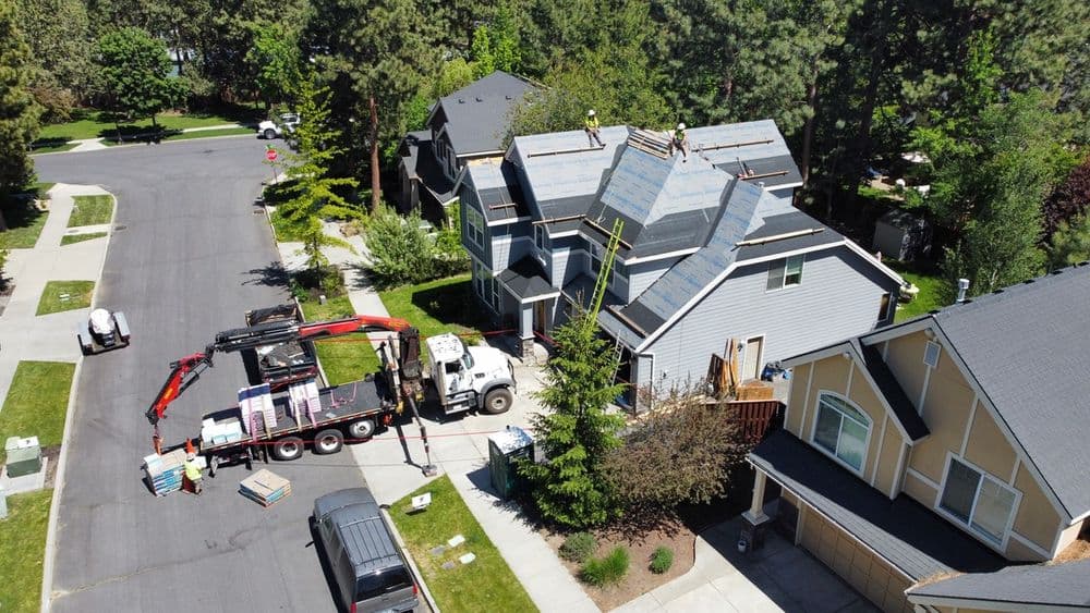 Aerial view of a house undergoing roof replacement with a truck delivering materials.