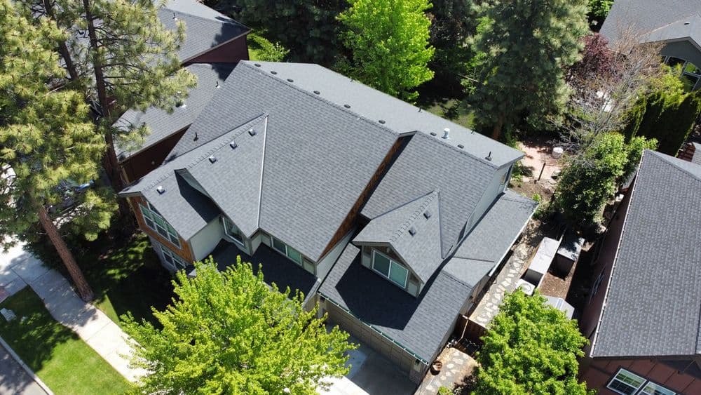 Aerial view of a modern house with a gray roof surrounded by lush green trees.