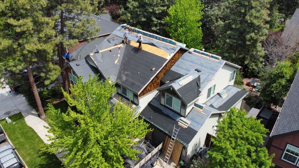 Aerial view of a house undergoing roof replacement with workers and greenery nearby.